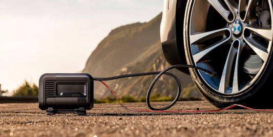 Noco AIR15 - 15A 80PSI Portable Tyre Inflator connected to a car tyre on a scenic roadside, ideal for inflating tires up to 33 inches.