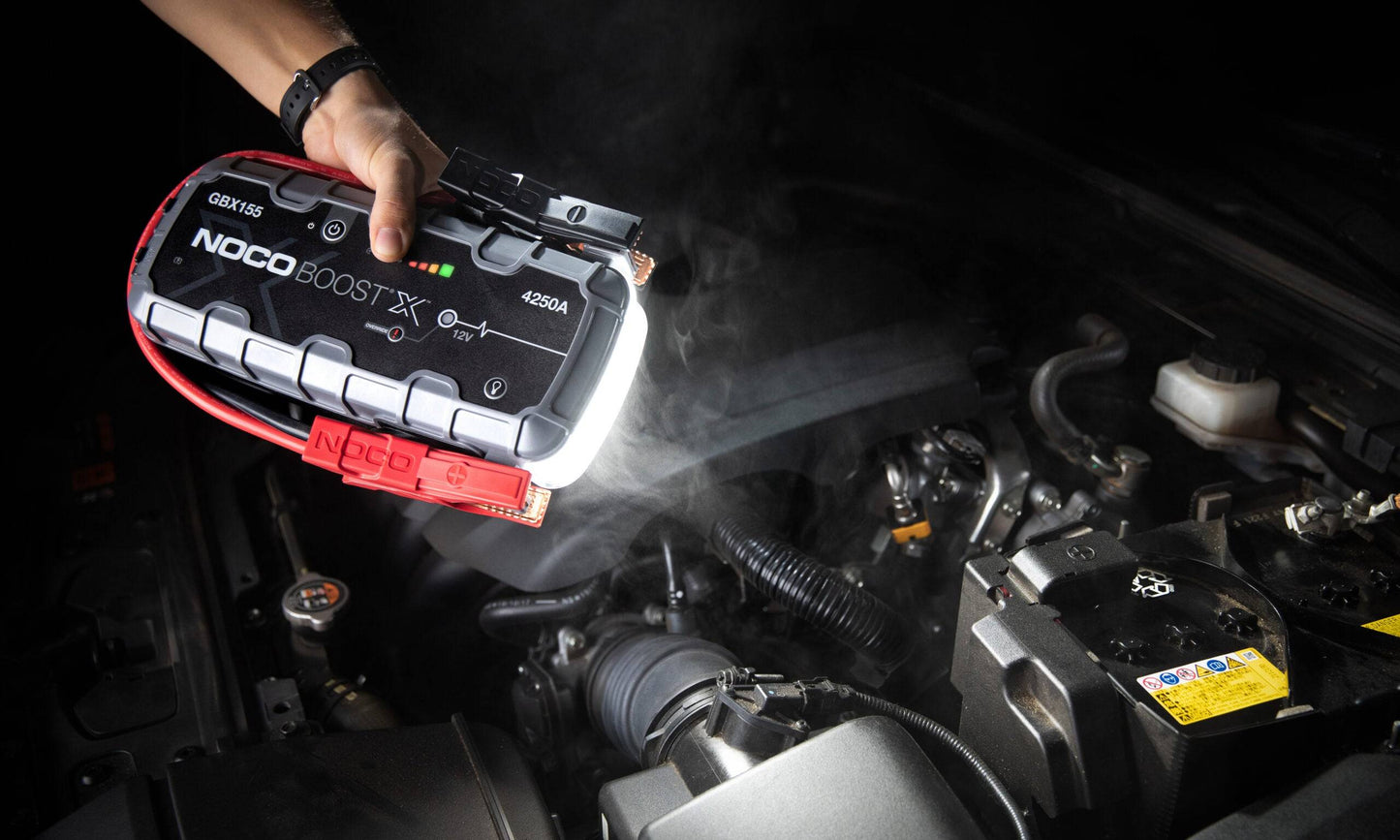 Noco Boost X GBX155 4250A jump starter with built-in LED light illuminating a car engine bay, designed for night-time or low-light vehicle repairs.