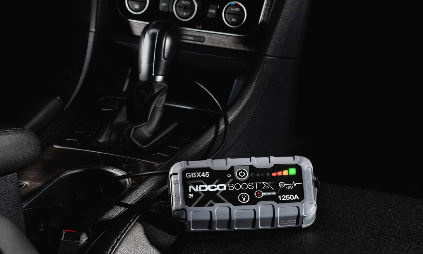 Noco Boost X GBX45 Lithium jump starter Boost Pack 1250A charging inside a car, ideal for 6.5L petrol and 4.0L diesel engines. Compact and powerful vehicle accessory.