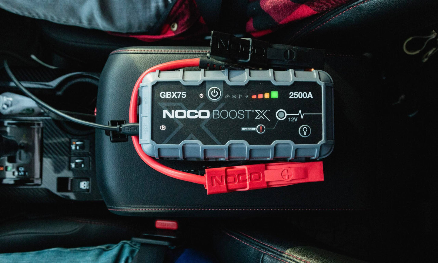 Noco Boost X GBX75 2500A Extreme Power Jump Starter resting on a car's center console, showcasing its rugged design and USB-C fast charging feature.